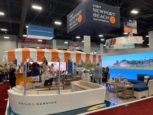 Trade show booth for Newport Beach, California, featuring beach-themed decor, informational displays, and seating area.