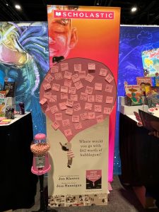 A Scholastic display with a large balloon covered in sticky notes, promoting the book "Abner and the Bubblegum Balloon" by Jon Klassen and Jess Hannigan. A gumball machine is in front of the display.