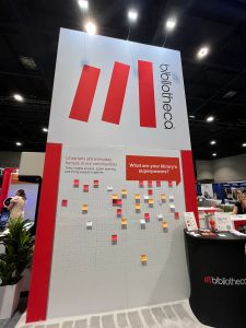 A tall display board at a trade show asks, "What are your library's superpowers?" with colored sticky notes attached to a grid below the question.