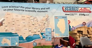 Science America booth with a U.S. map display, encouraging people to pin their favorite scientific moment; boxes, maps, and promotional signs are visible.